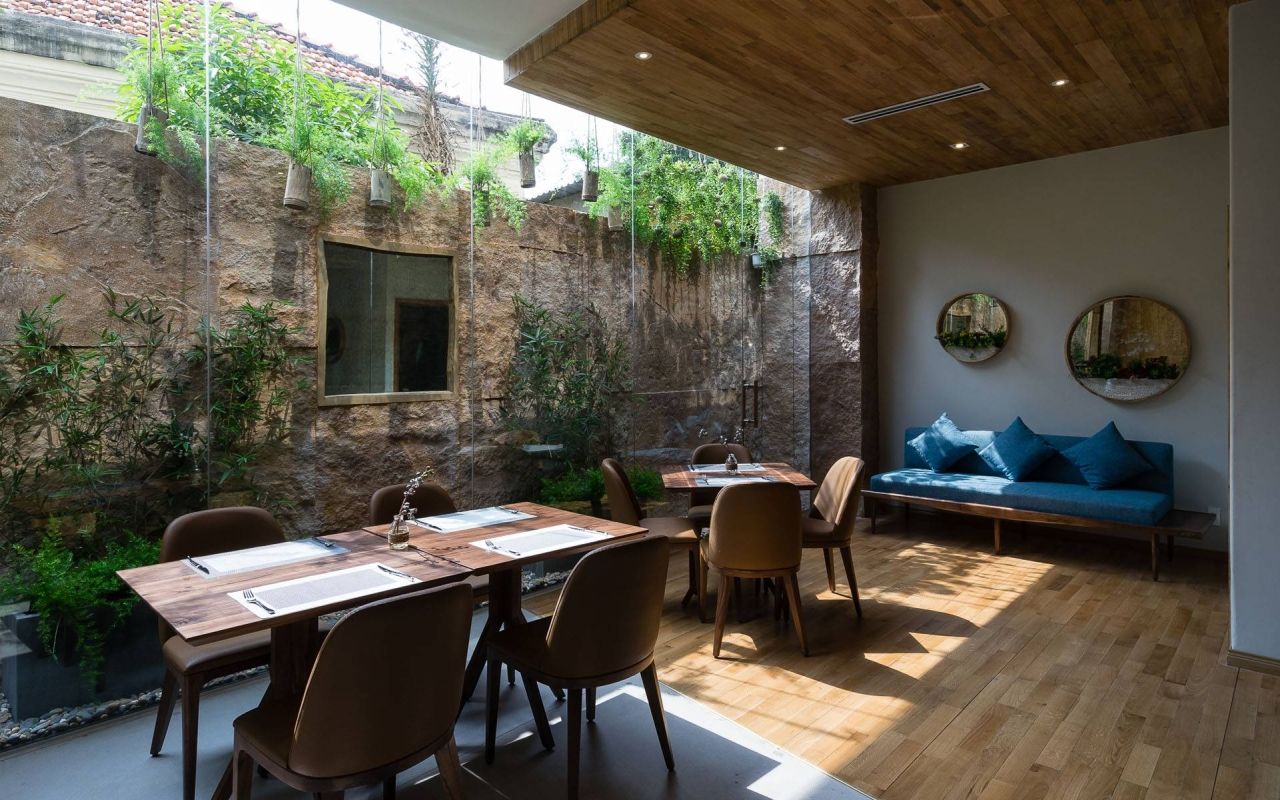 Yen Rooftop Bar: An Award-Winning Rooftop Bar in District 1 5 Yen Restaurant on the ground floor of Silverland Yen in daylight, with timber tables and a planted courtyard wall